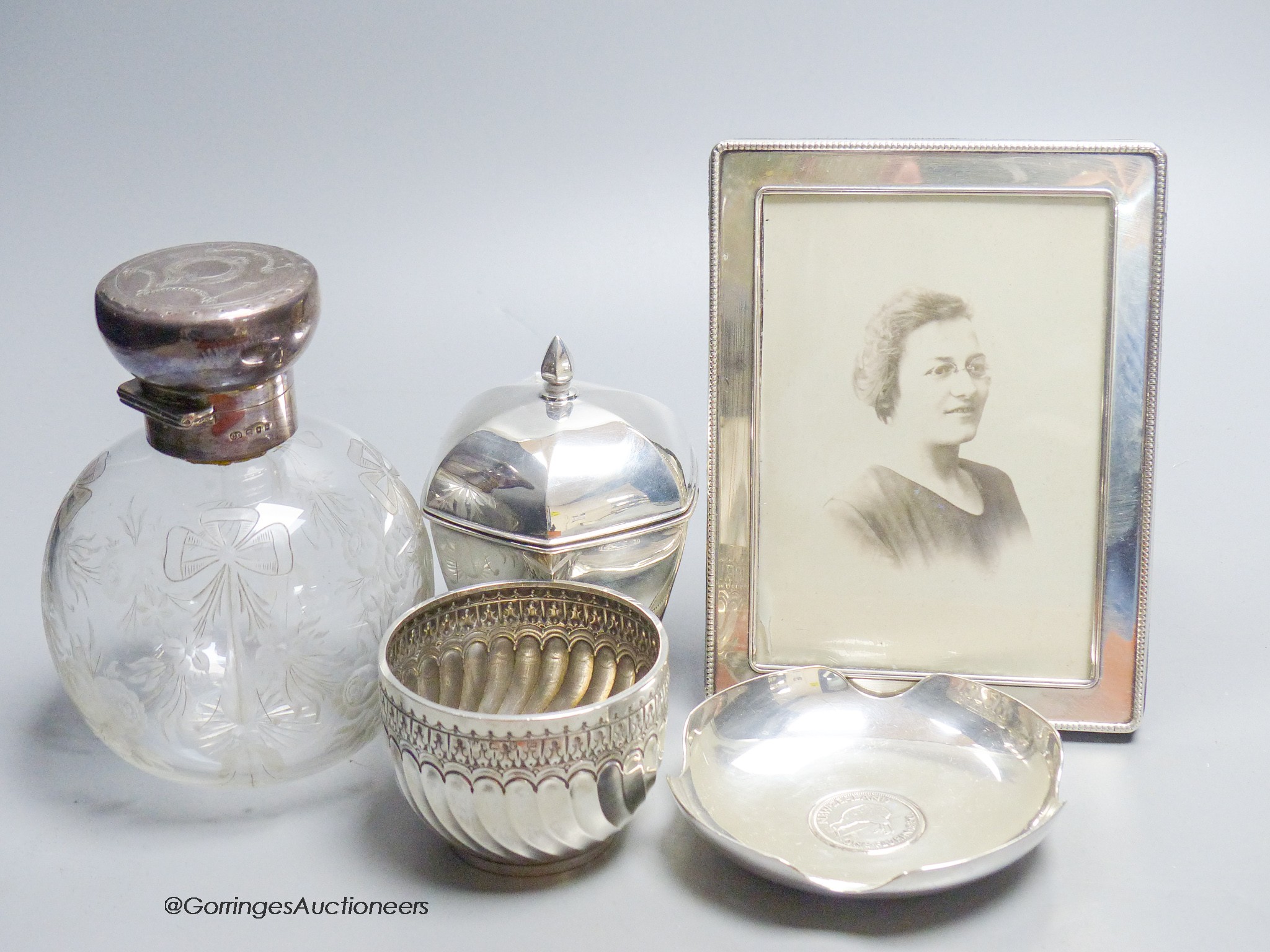 A George V panelled silver tea caddy, Sheffield, 1918, 10.2cm, a late Victorian silver bowl, a silver mounted glass scent bottle, a modern silver mounted photograph frame and a plated coin dish.